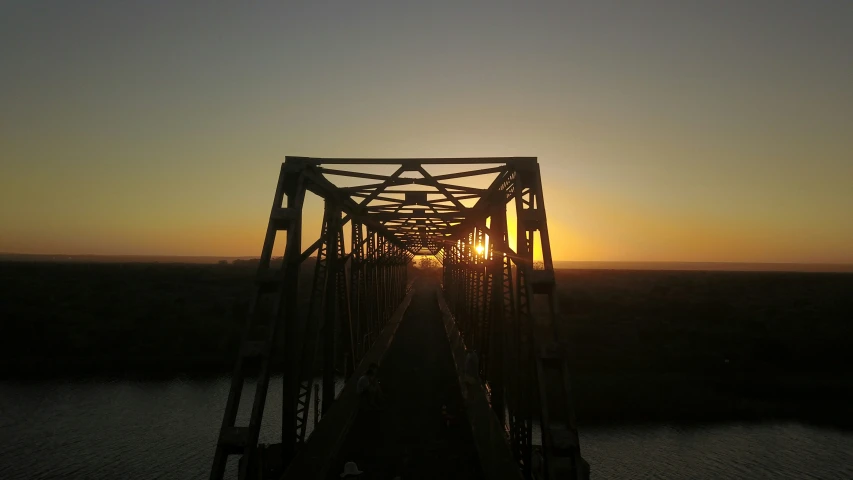 the sun is rising over an old steel bridge