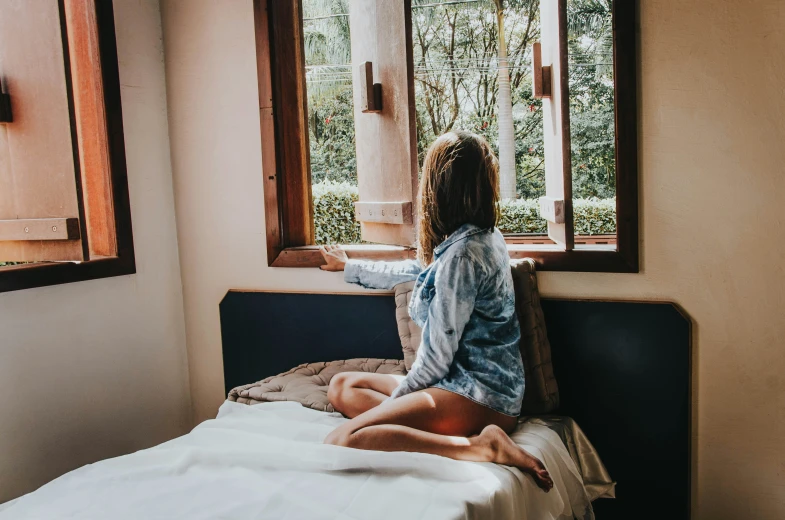 a woman sitting on a bed looking out a window