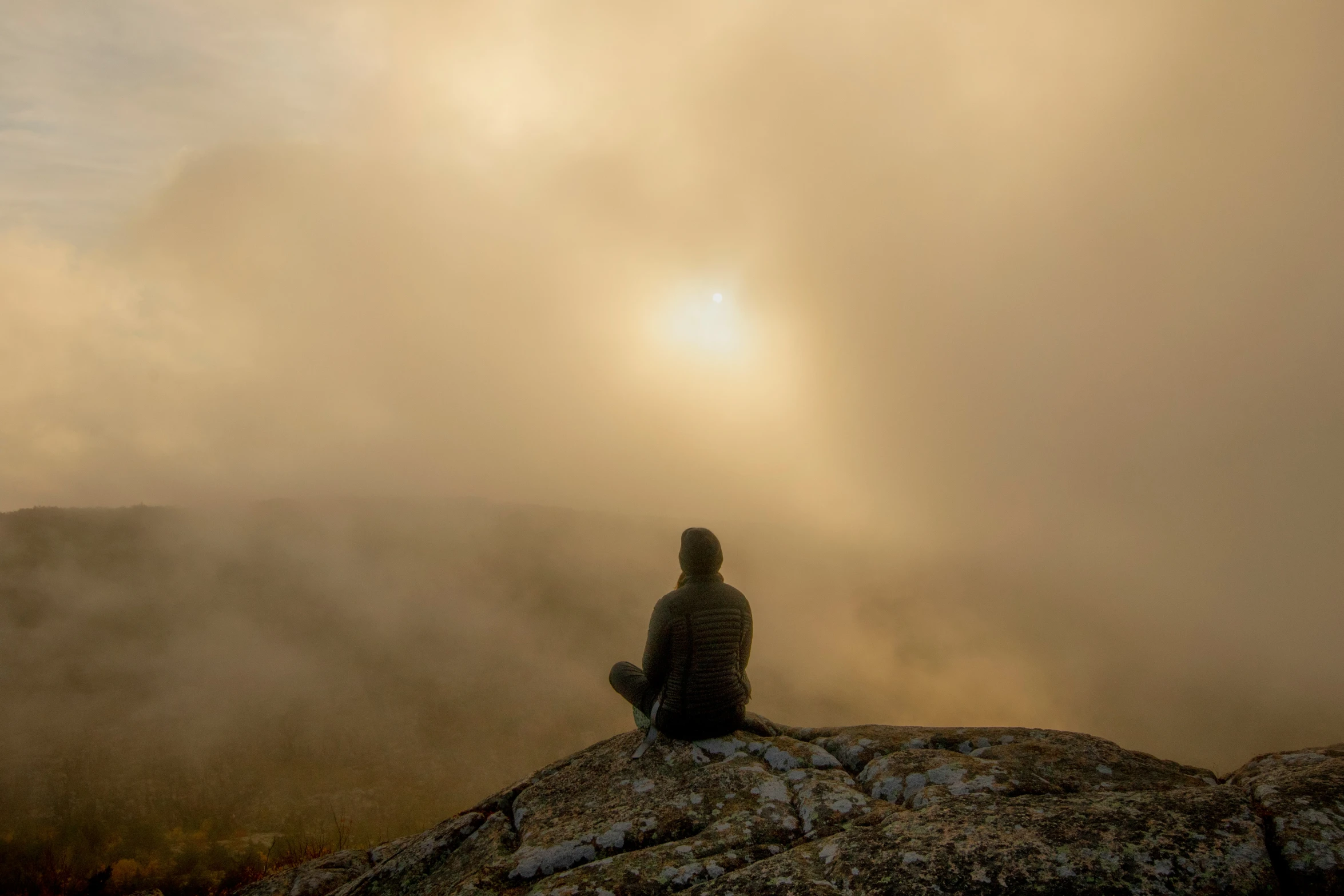 a man in the fog is sitting on a rock with his back turned