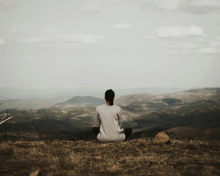 a woman sitting on the ground looking out into mountains