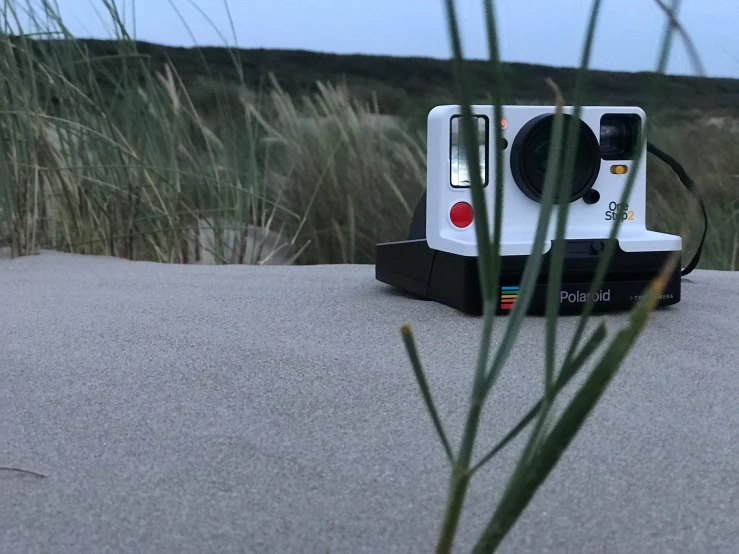 there is a polaroid camera left on the beach by the grass