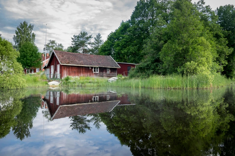 an old red cabin on a lake near a forest