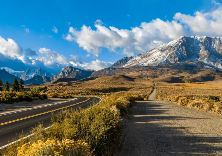 a road running through a meadow with mountains in the background