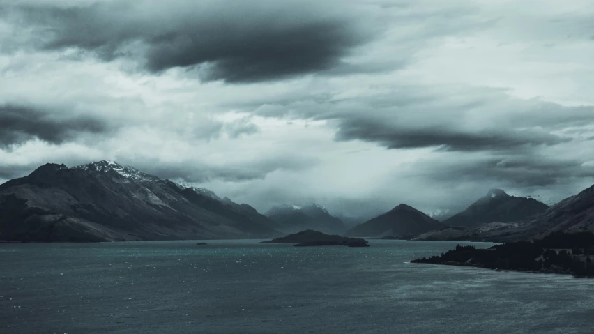 some trees and mountains with clouds on a lake