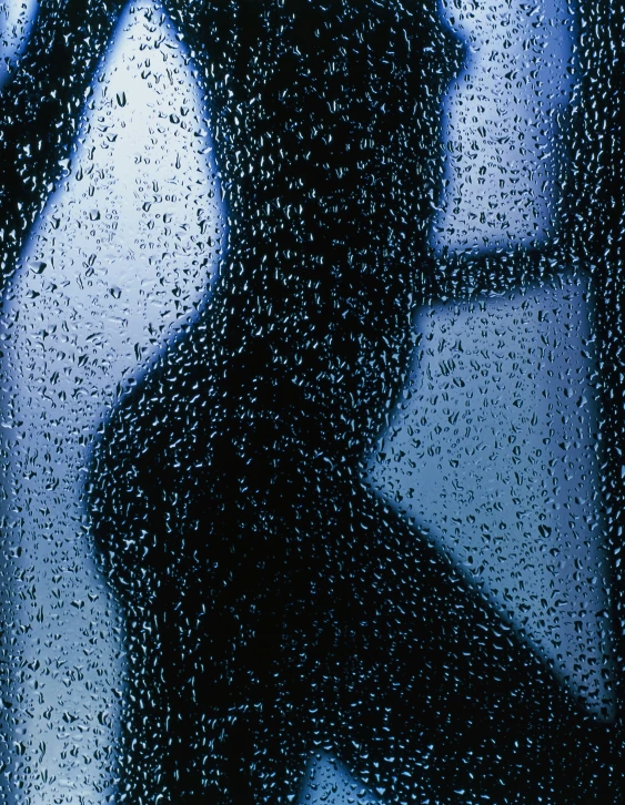 rain drops all over a window as a person walks