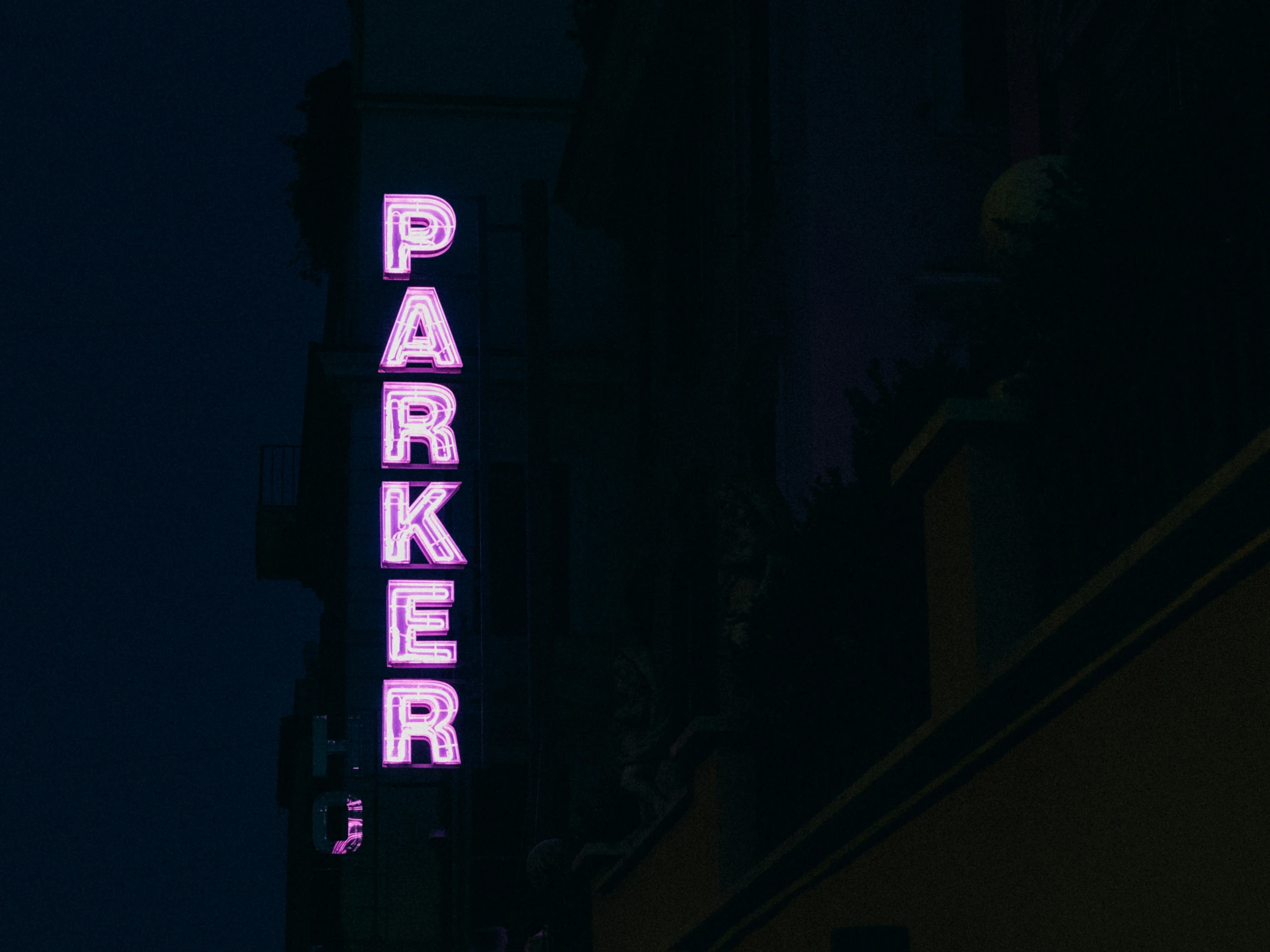 a pink and green neon sign hanging from the side of a building