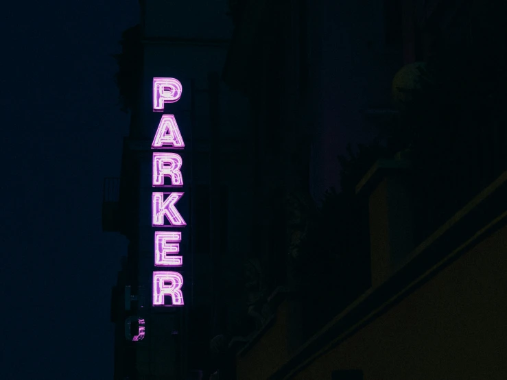 a pink and green neon sign hanging from the side of a building