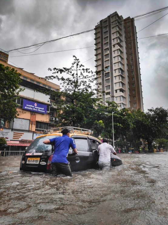 a couple of people hing a vehicle through flood waters