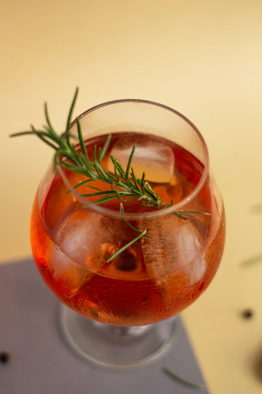 a wine glass filled with a clear red liquid and a green sprig