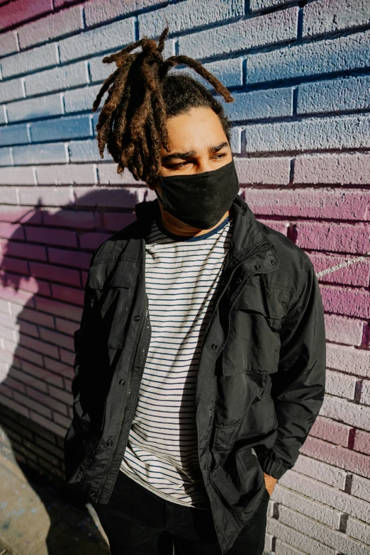 a young man with dreadlocks wears a black cloth face mask