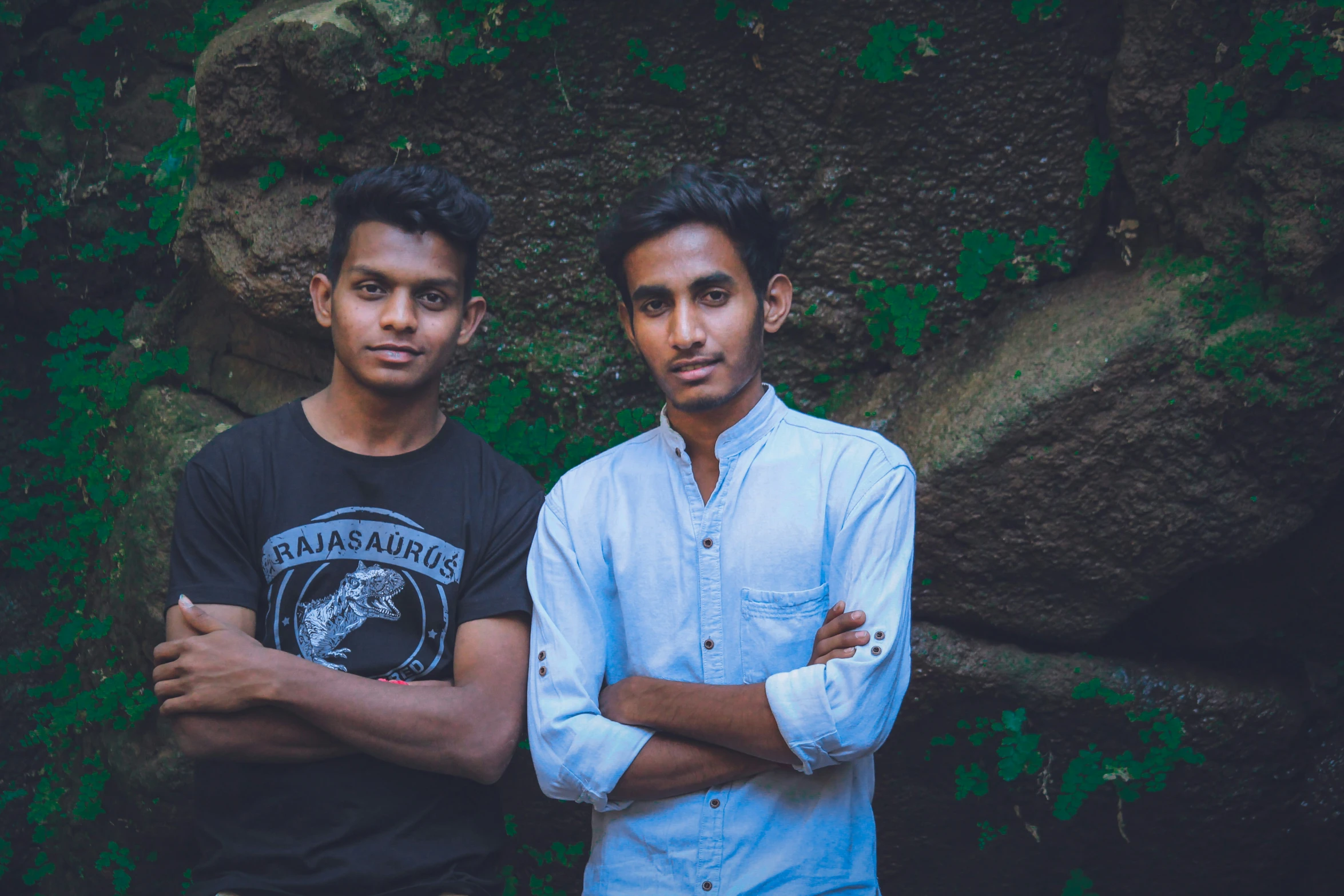 two young men posing for a po in front of a moss covered rock