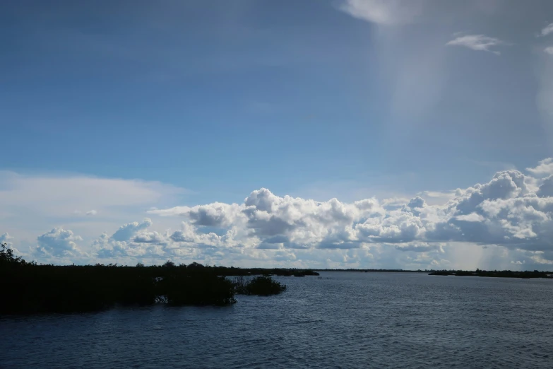 clouds and water with a distant plane flying over it