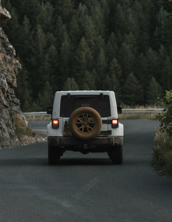 white jeep with gold rims driving down a narrow road