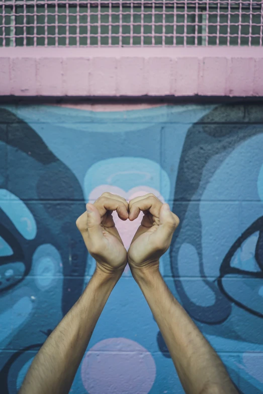 two hands covering a heart against a blue painted wall