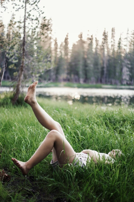 a woman laying in some tall grass and trees