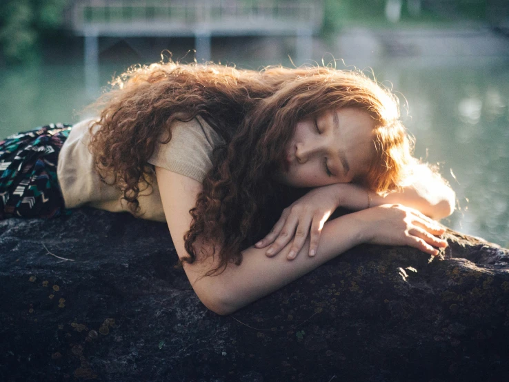 the woman is laying on a rock with her head resting on her arms