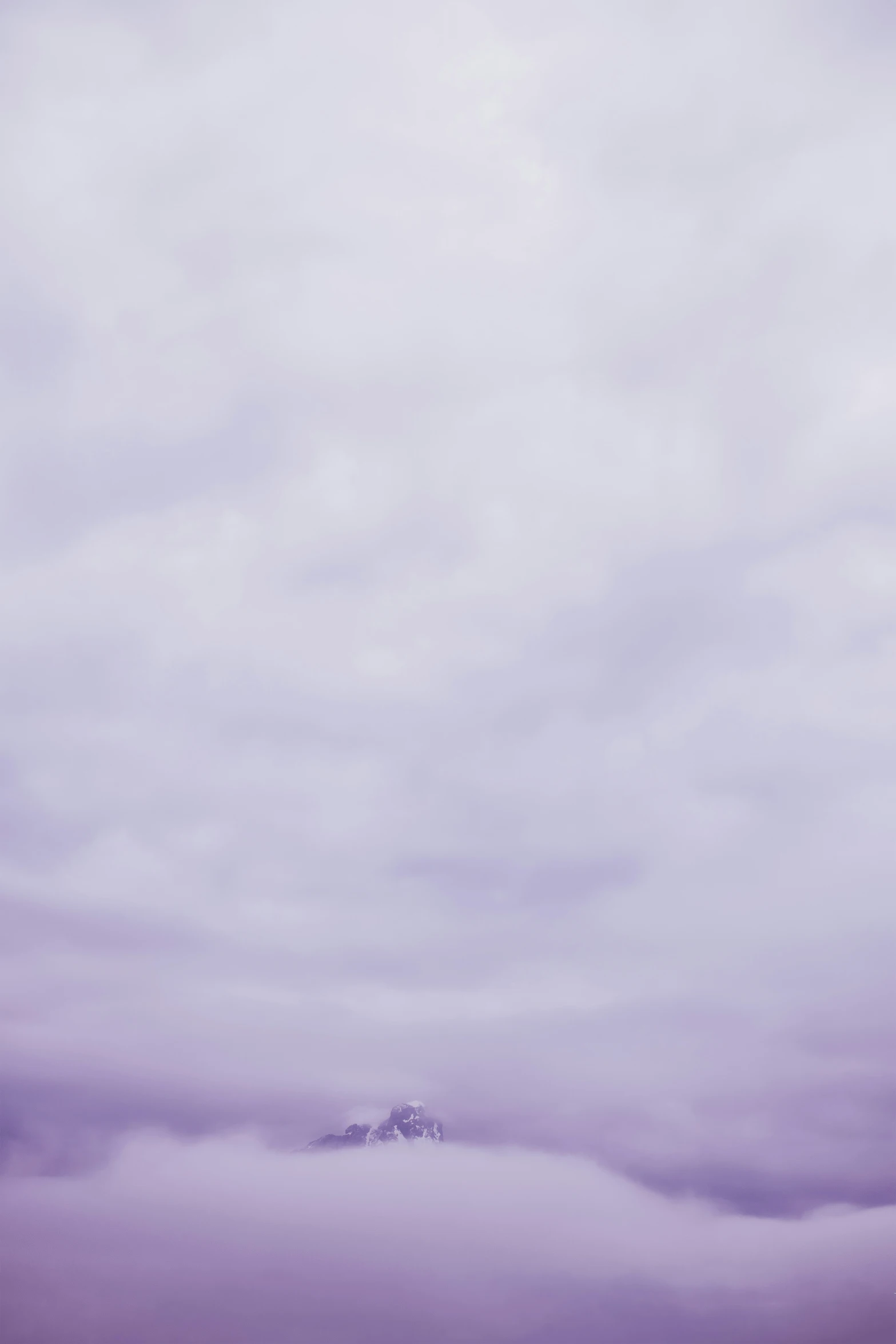 a single snowy mountain in the distance, surrounded by low lying clouds