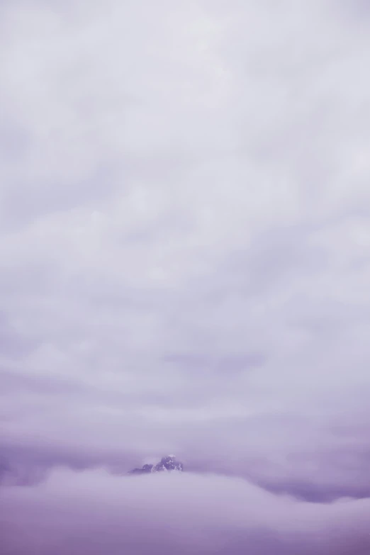 a single snowy mountain in the distance, surrounded by low lying clouds