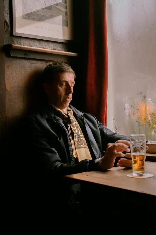 a man sitting at a table with a glass and flower vase