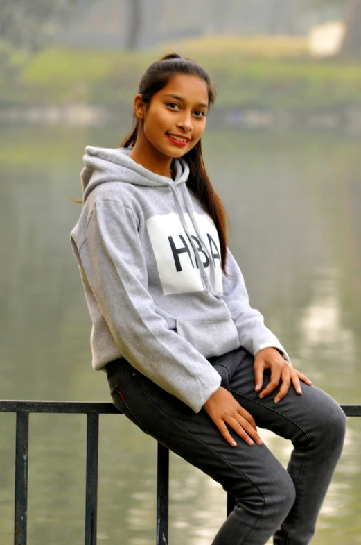 a woman sitting on top of a fence near a body of water