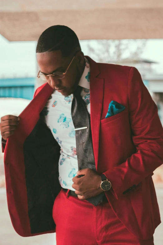 a man in a red suit jacket looking down and reading his watch