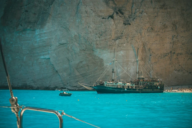 two ships sitting near the shoreline next to a large cliff