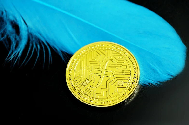 a gold coin sitting in front of a feather