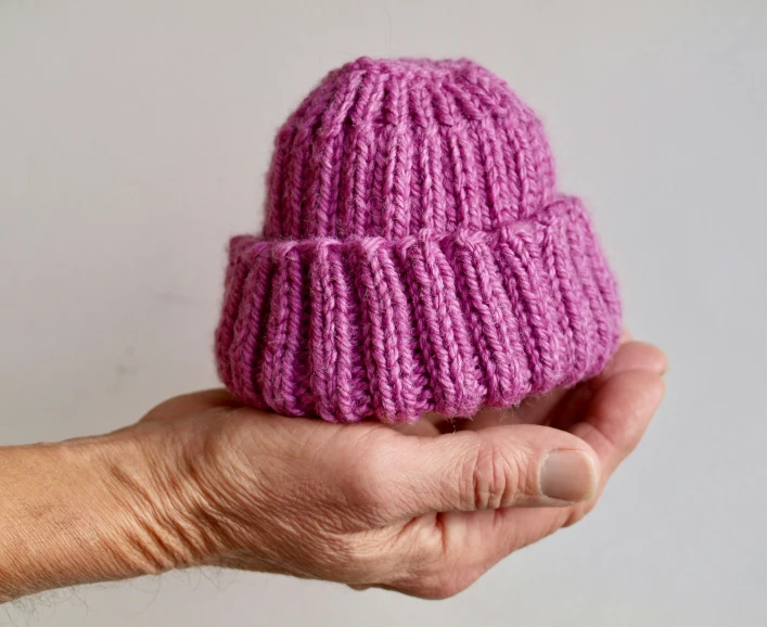 the hand is holding a knitted pink hat