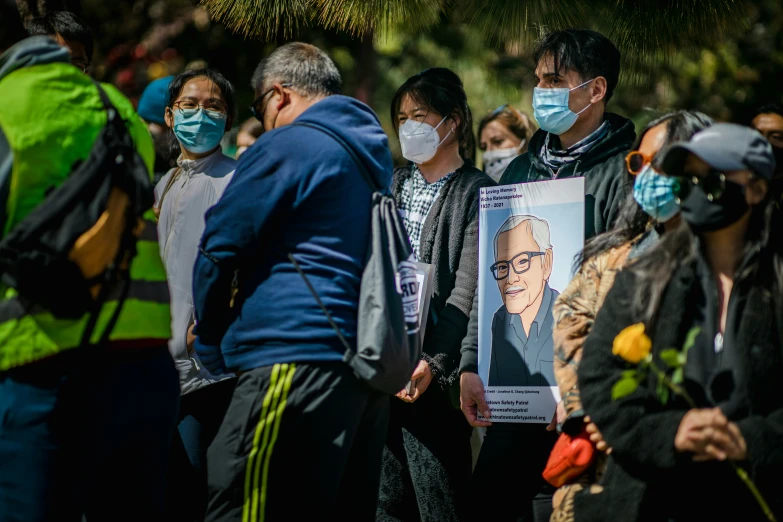 a large group of people wearing face masks stand next to a sign