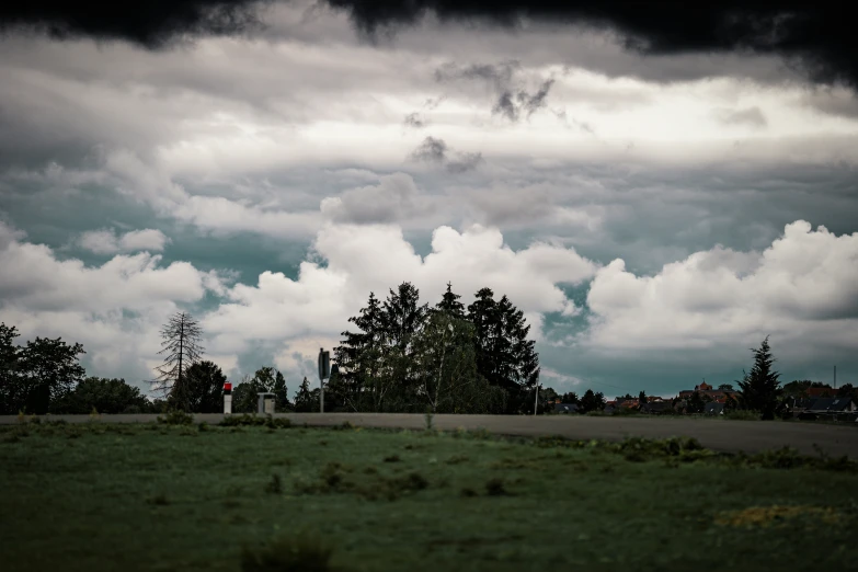 an empty parking lot with a green grass field on the other side, and a dark and cloudy sky in the distance