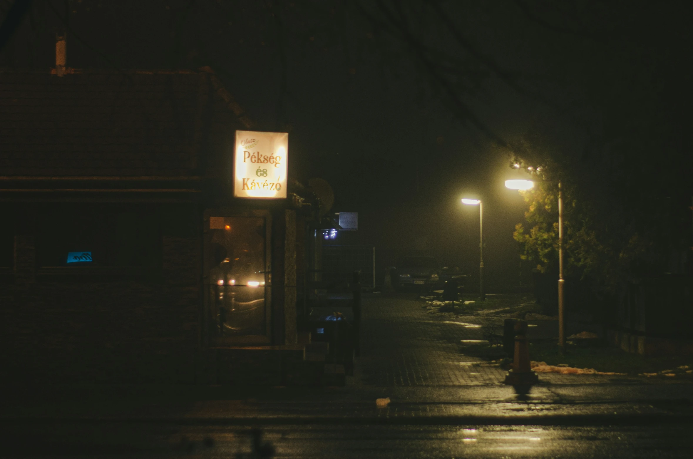 a dark street is seen at night, with a sign lit up