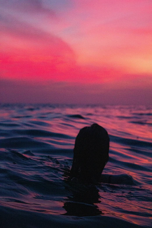 the silhouette of a person is at the water's edge as dusk lights up the sky