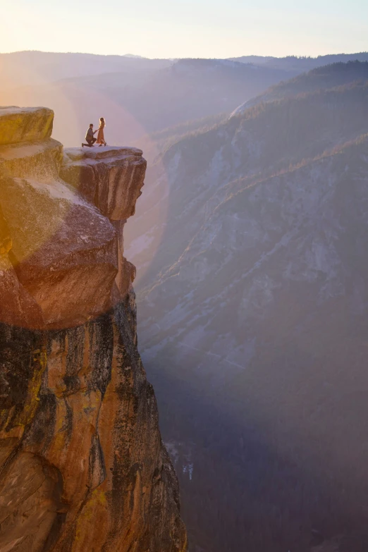 two people sitting on a cliff with the view looking out at the valley