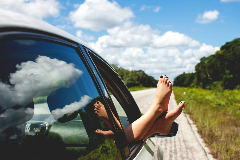 person's feet sticking out of car window and sky reflected in rear view mirror