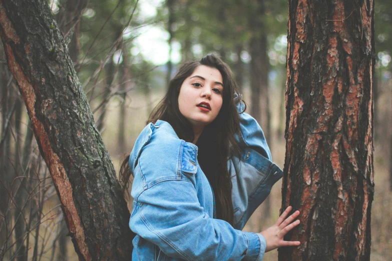 the girl is standing near the trees with her head up