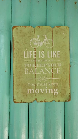 a sign on a blue wooden wall stating that life is like riding a bike