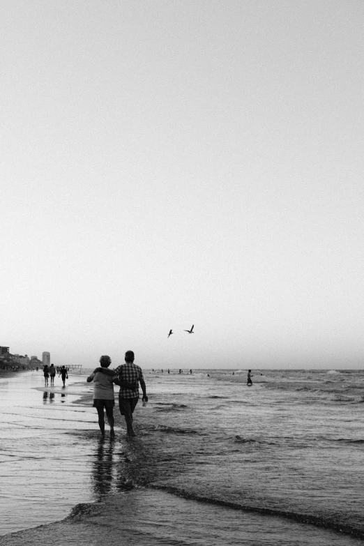 several people walk on a sandy beach towards the water