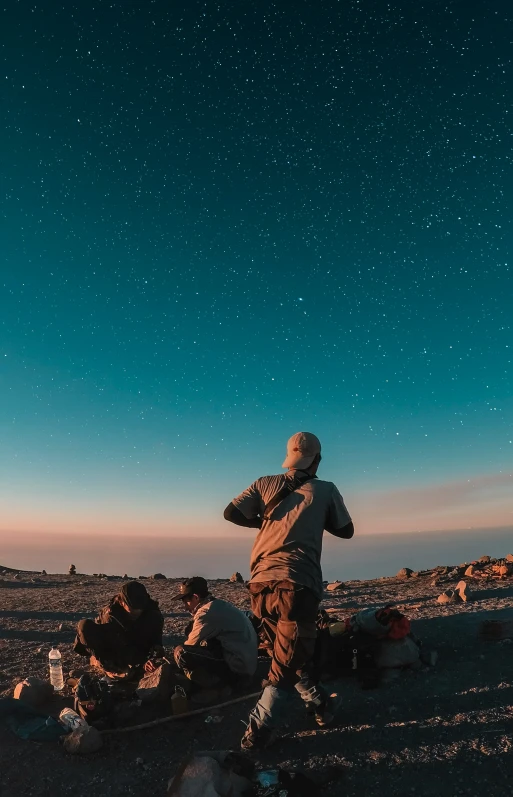 man standing on rocks watching night sky with stars in distance