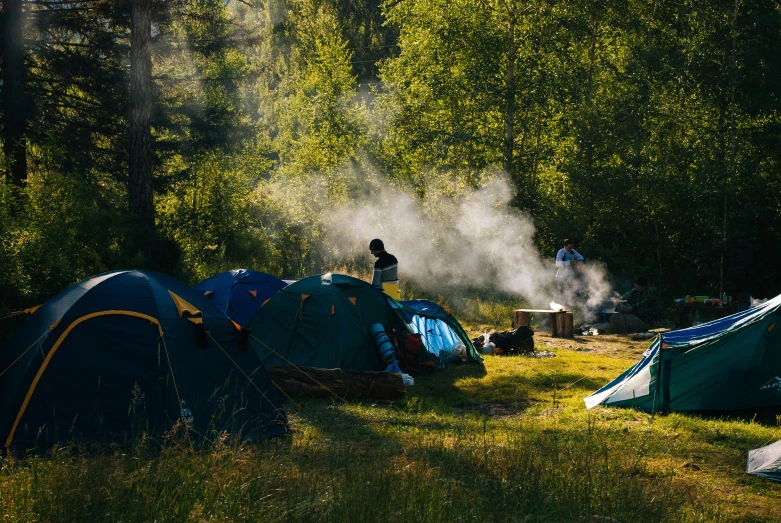 a group of tents in the forest with mist coming from them