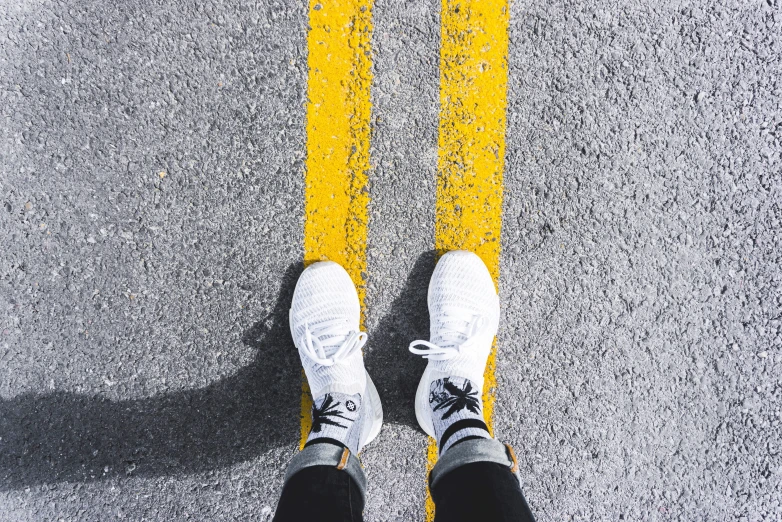 a person in white sneakers standing on an asphalt road