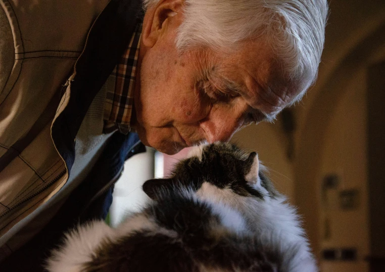 an old man holding a small cat up to his face