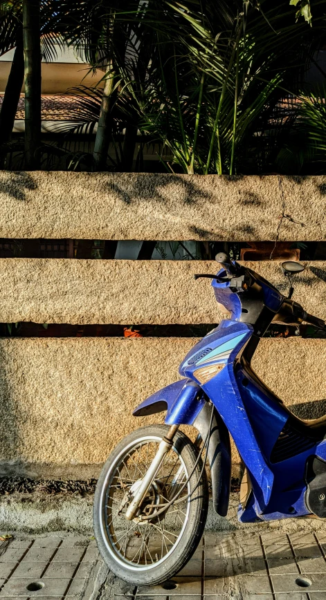 a blue motorbike parked next to the wall of the building
