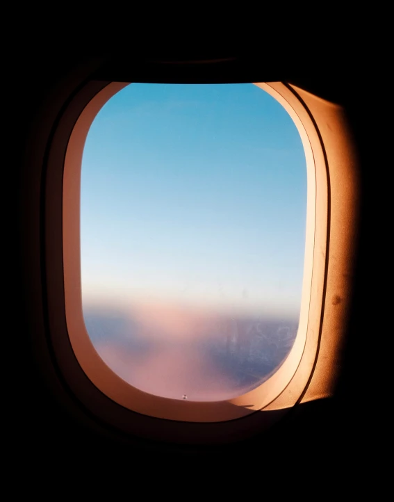 an airplane window as the sun sets and the clouds are seen