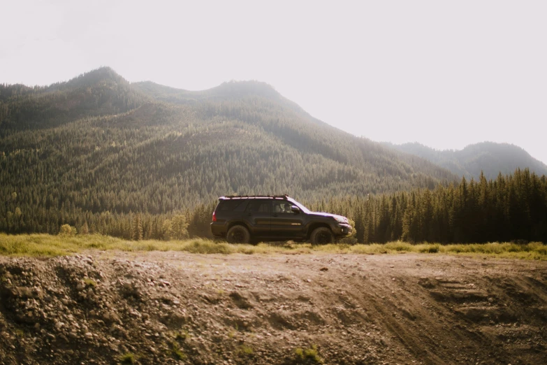 the truck is parked in the dirt with trees behind