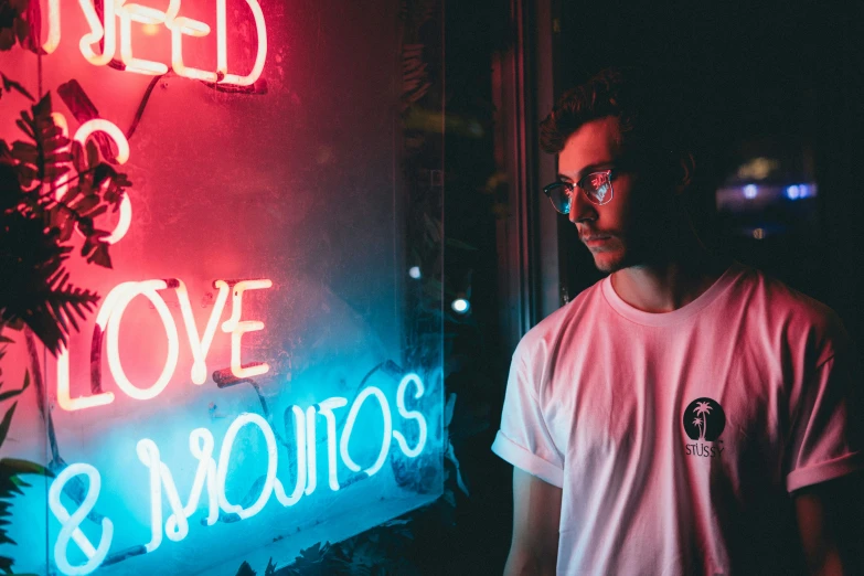 man wearing eye glasses looking off into distance in front of a neon sign that says love and romas