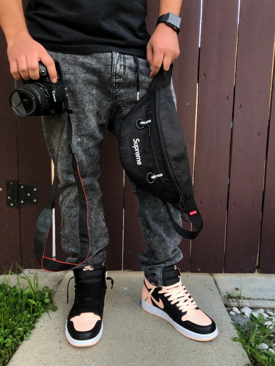 person standing on sidewalk holding a camera and backpack