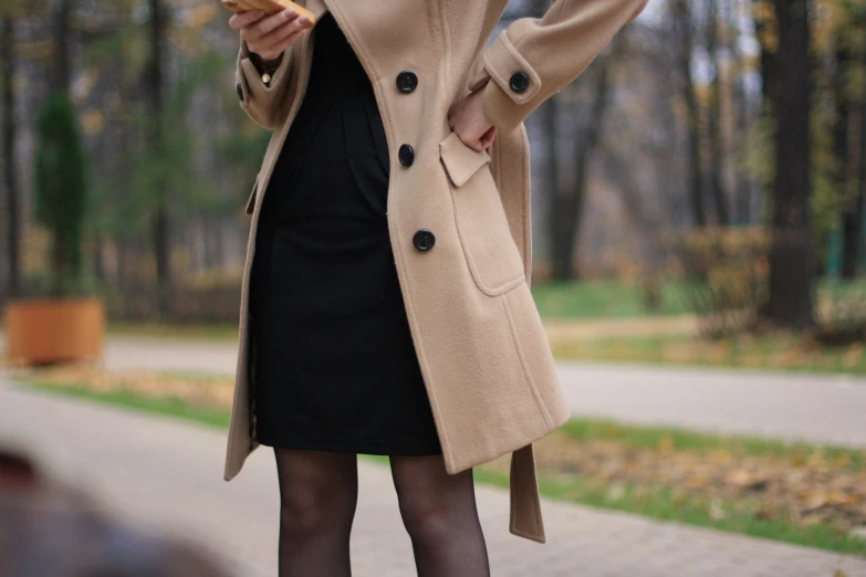 a young woman in black tights, a tan coat and brown shoes eating a donut