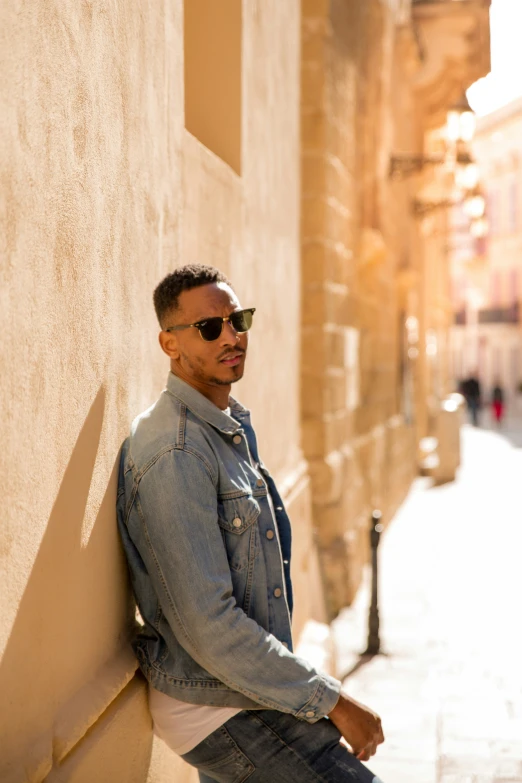 man in sunglasses leaning against a stucco wall