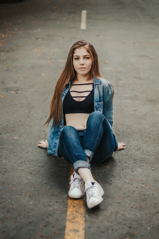 a girl sitting in the middle of a road with her arms out