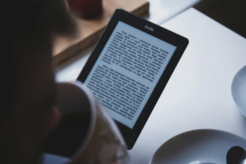 a hand holding a kindle with a book on it next to cups